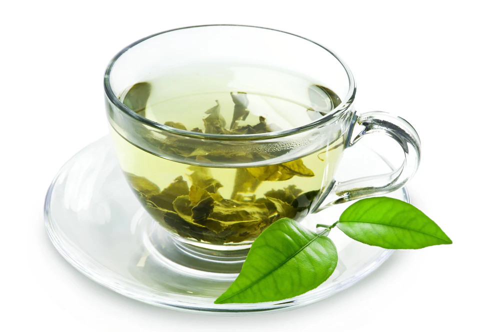 Üvegpohárnyi zöld tea szálas tealevelekkel (gőzölgés nélkül), valamint friss zöld levelek a csészealjon.