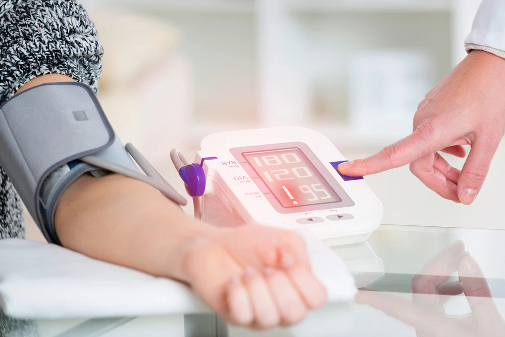 Vérnyomásmérő mandzsetta egy ember karján, miközben egy kéz a mérési eredményeket mutató digitális kijelzőt állítja be.