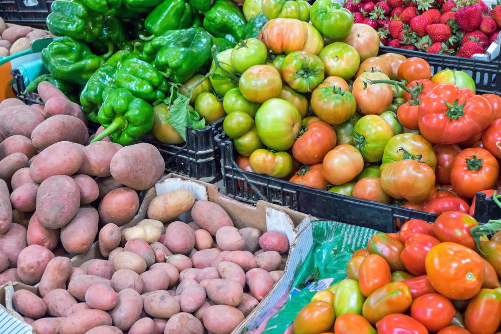 Vegyes friss zöldségek piaci ládákban: zöldpaprika, paradicsom, burgonya és eper.