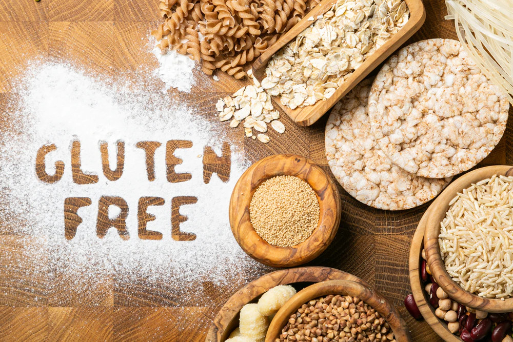 Különféle gabonafélék és tésztafélék fa deszkákon; lisztből kirakva a „GLUTEN FREE” (gluténmentes) felirat.